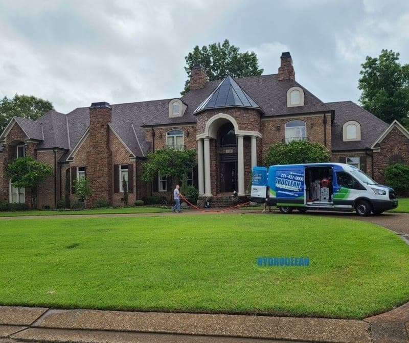 HydroClean van parked in front of a large brick home, with a hose run to the front door